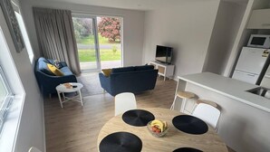 Un salon moderne avec une table de salle à manger ronde en bois, des chaises blanches, un canapé bleu et un téléviseur.