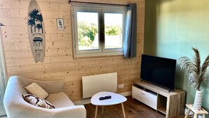A cozy room with a wooden wall, a surfboard decoration, a television, a sofa, a small table, and a plant. - Chalet - Terrasse & bain nordique (Trégastel)