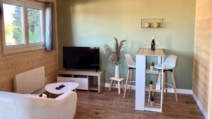 A cozy living room with a wooden ceiling, a flat-screen TV, a dining table with chairs, and a sofa. - Chalet - Terrasse & bain nordique (Trégastel)