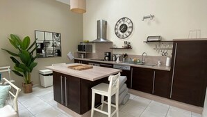 Una cocina moderna con una isla central, un comedor con una silla de mimbre y un amplio ventanal que proporciona luz natural.