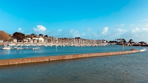 Una marina costera con barcos amarrados, un rompeolas de piedra y edificios al fondo.