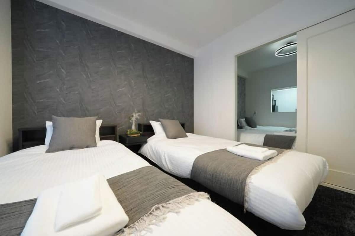 Quarto de hotel com duas camas, parede escura com textura, um espelho e uma luminária moderna.