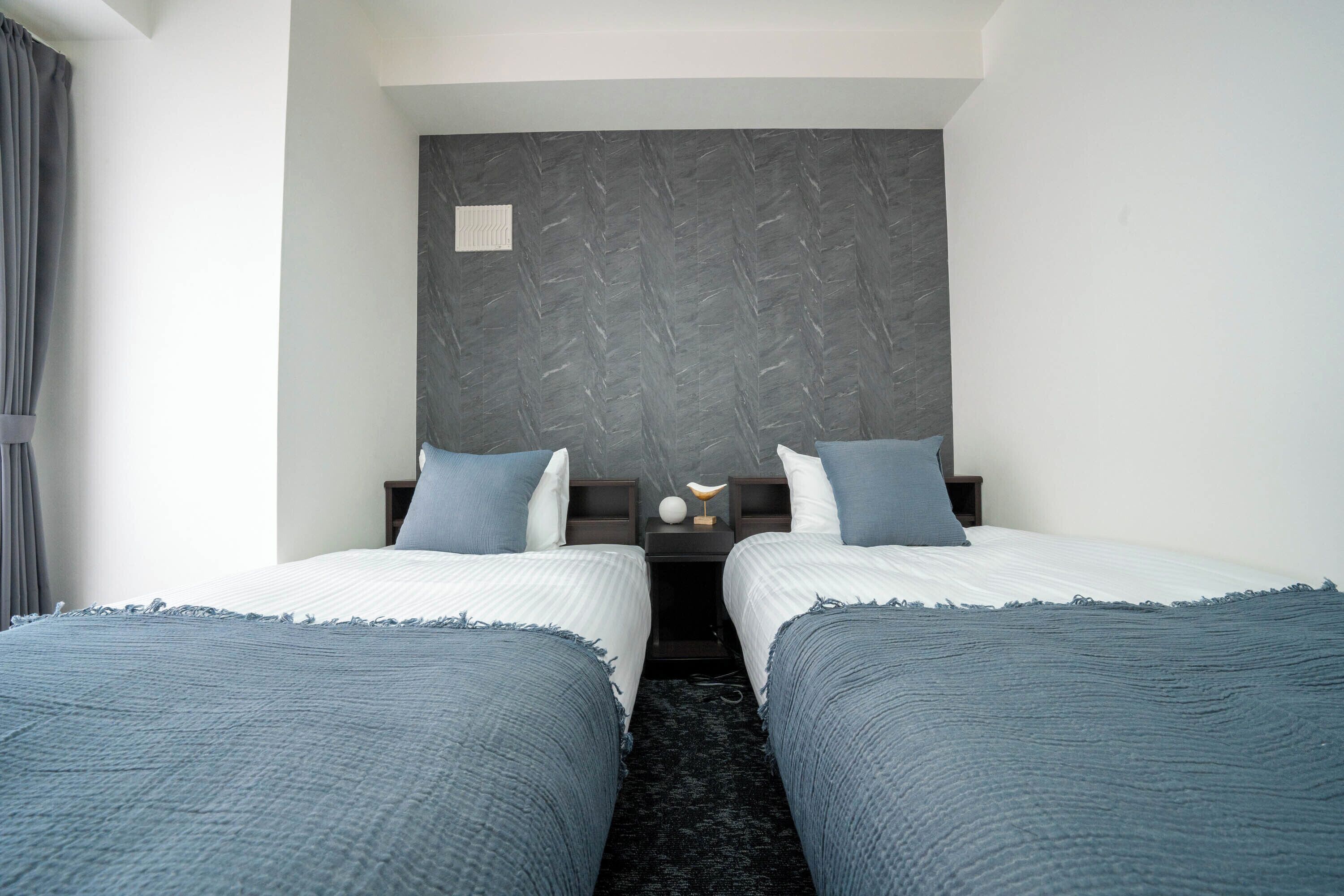 A hotel room with two beds, a dark headboard, and a small bedside table with a lamp.