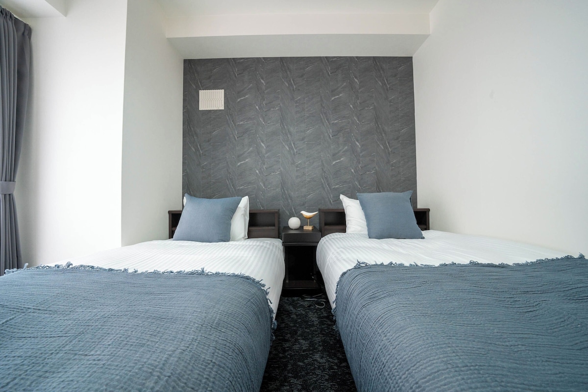 A hotel room with two beds, a dark headboard, and a small bedside table with a lamp.
