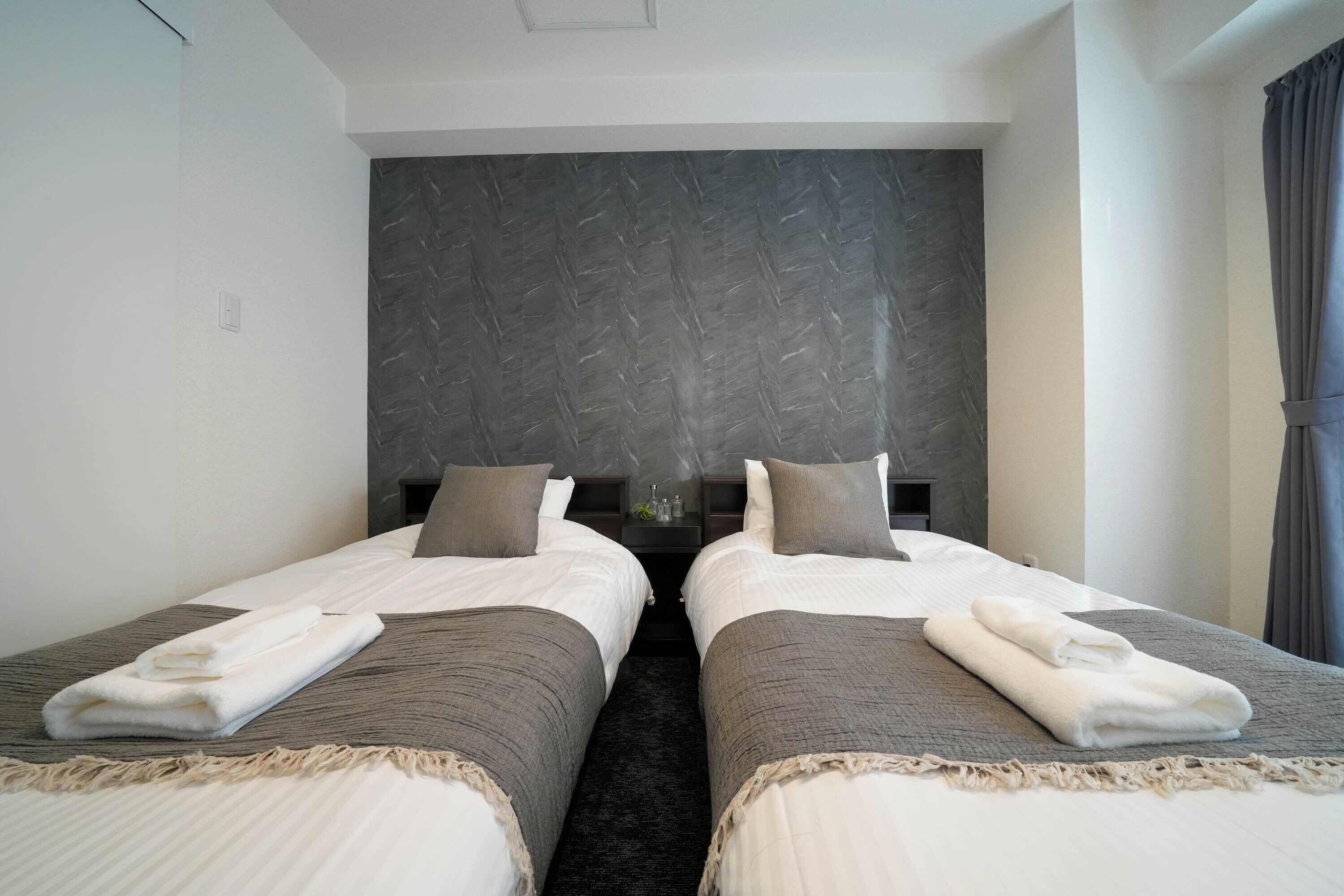 Una habitació d'hotel amb dos llits, cadascun amb un capçal de llit gris, roba de llit blanca i una tovallola doblegada sobre el llit.