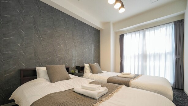 Habitación de hotel con dos camas, un amplio ventanal con cortinas, pared de mármol y una lámpara de techo moderna.