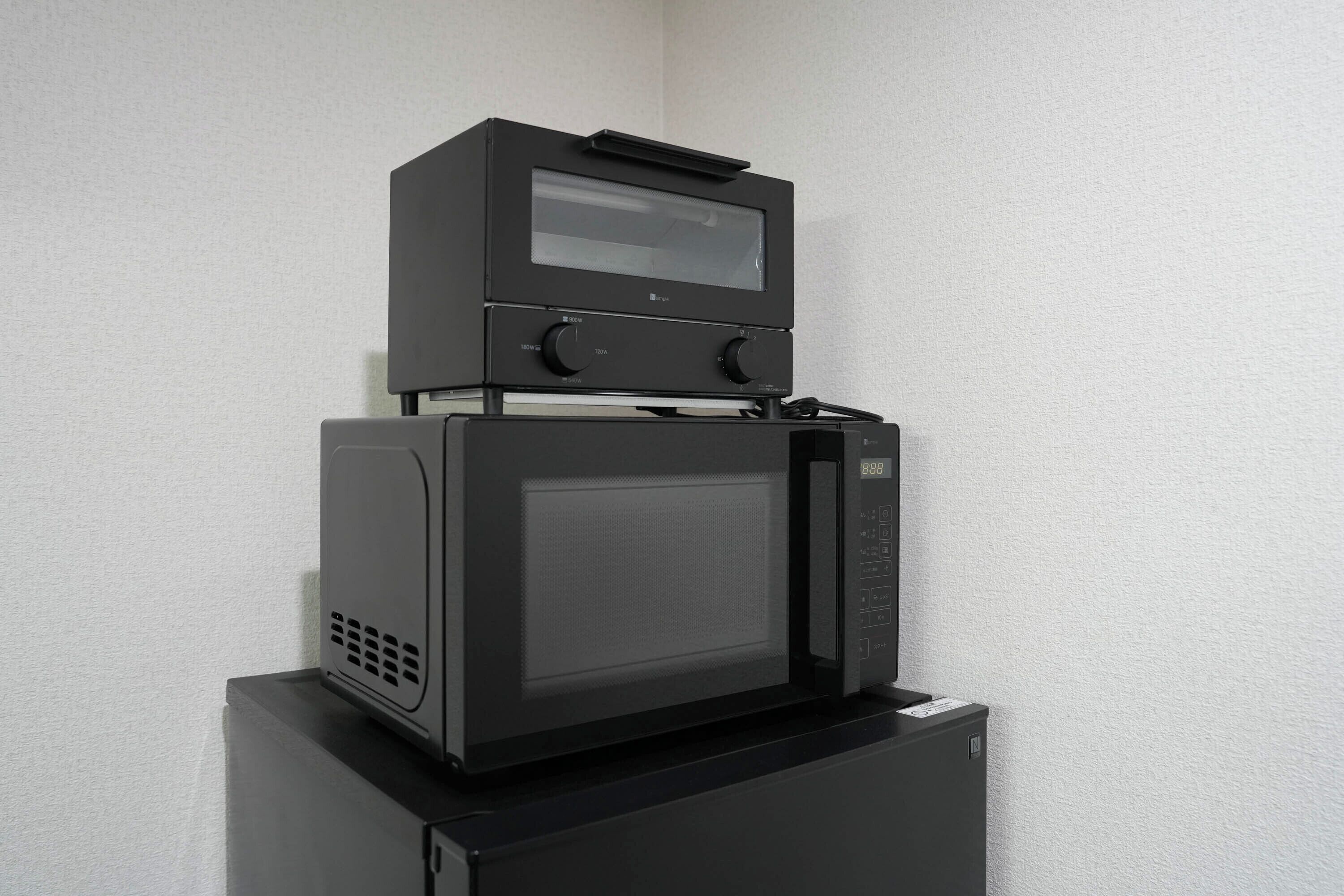 A black microwave oven with a digital display and a control panel, placed on top of a black refrigerator.