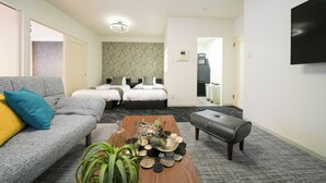 Habitación de hotel moderna con sofá gris, una mesa de centro de madera con objetos decorativos, un banco gris y una cama con ropa de cama blanca.