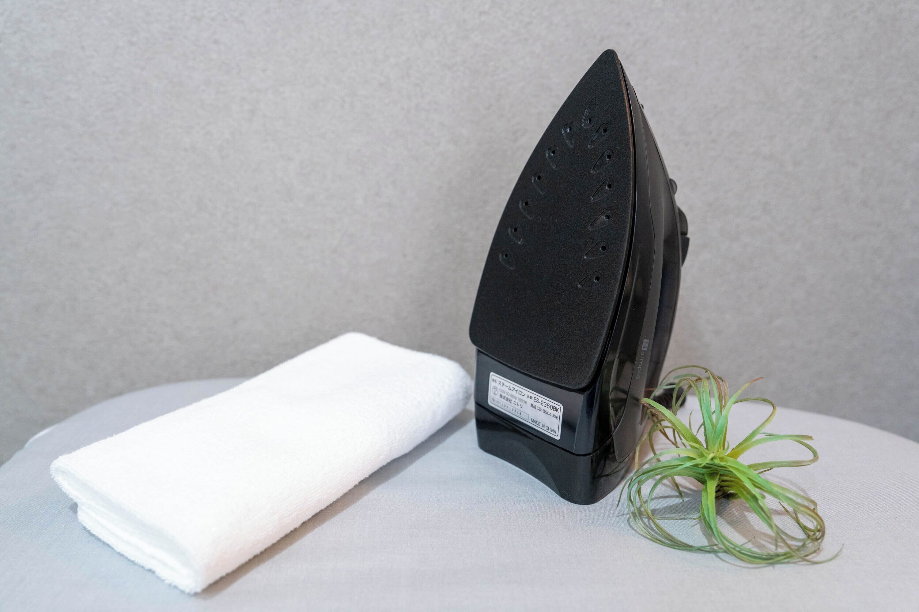 A black iron, a white towel, and a green plant on a white surface.