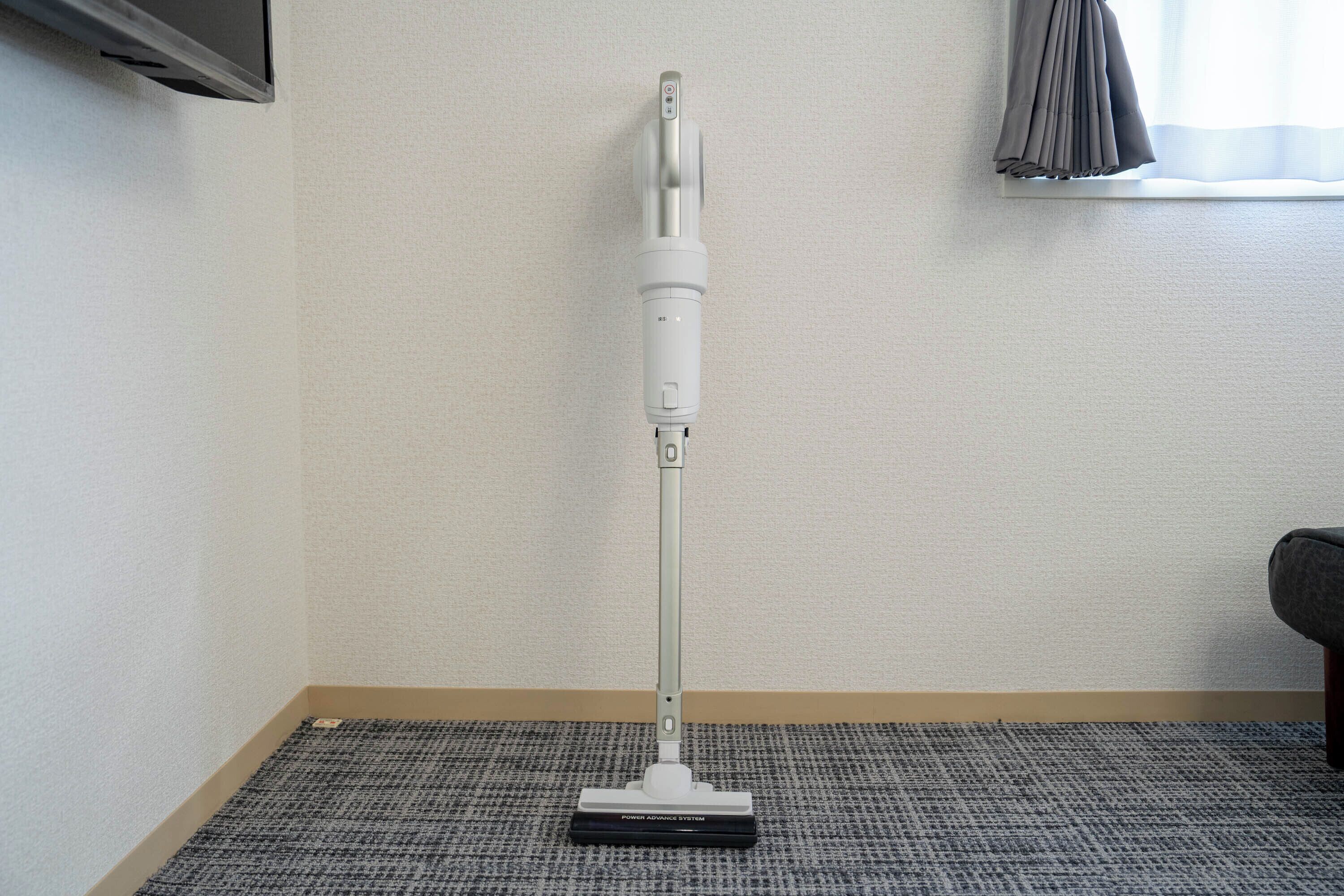 A standing vacuum cleaner in a room with a carpeted floor and a window with curtains.