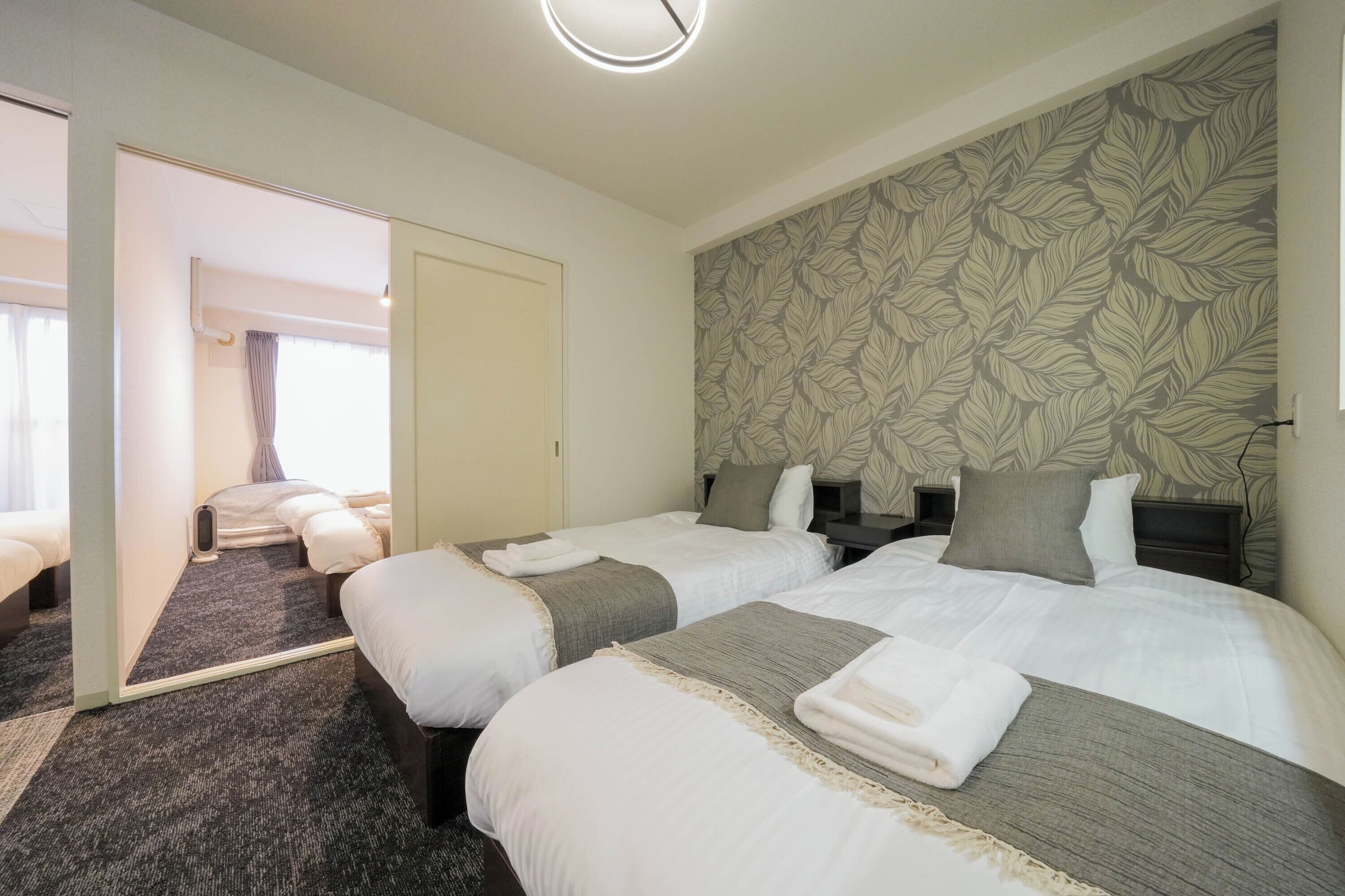 A hotel room with two beds, a large mirror, a floral-patterned wall, and a carpeted floor.