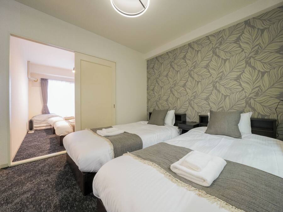A hotel room with two beds, a large mirror, a floral-patterned wall, and a carpeted floor.