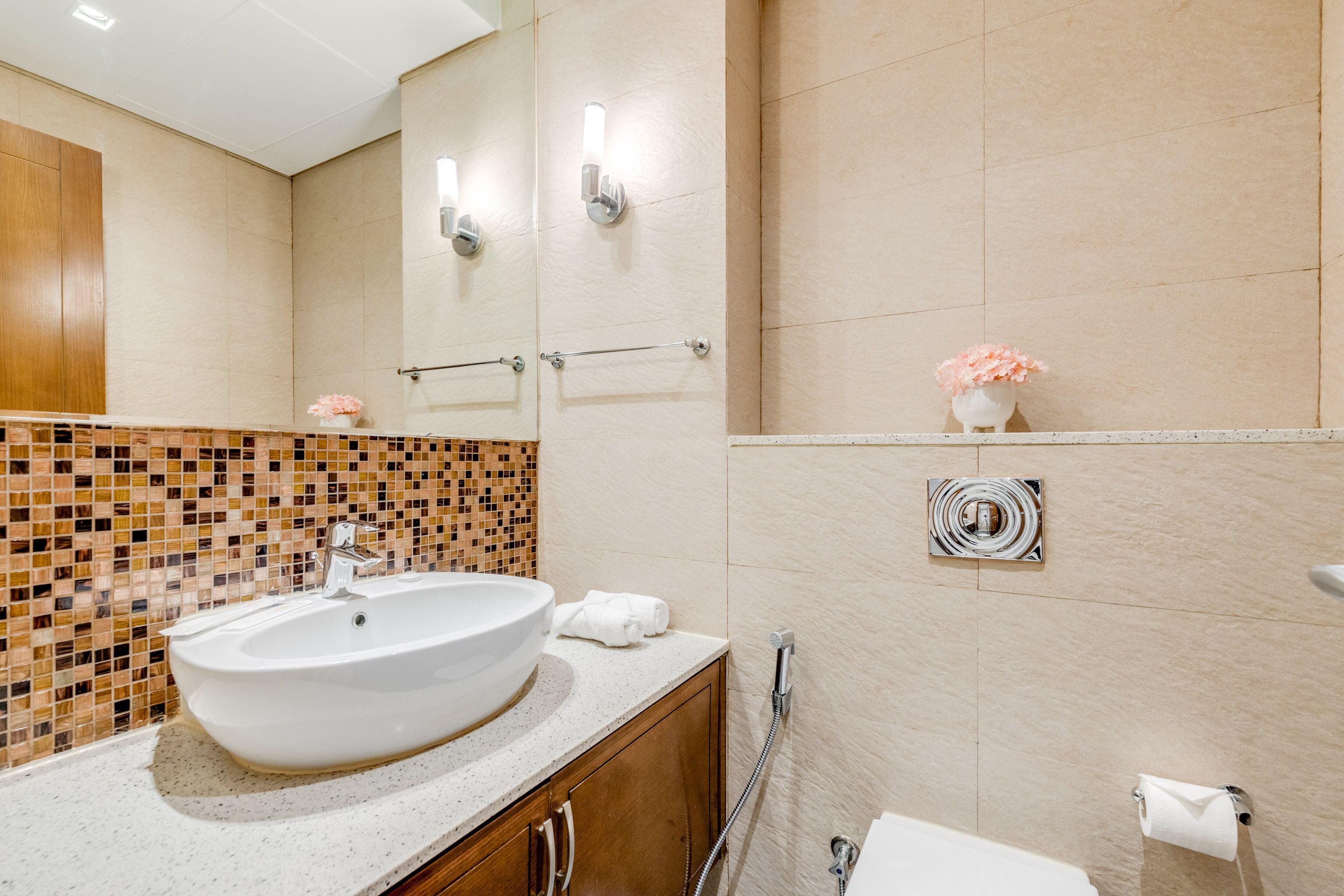 A bathroom with a white sink, a mirror, a towel rack, a toilet, and a small vase with flowers.