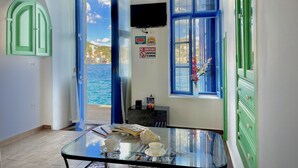 A room with a glass table, a view of the sea, a TV on the wall, and a 'No Smoking' sign. - Pitini 2 - Seafront - Harbour view (Symi)