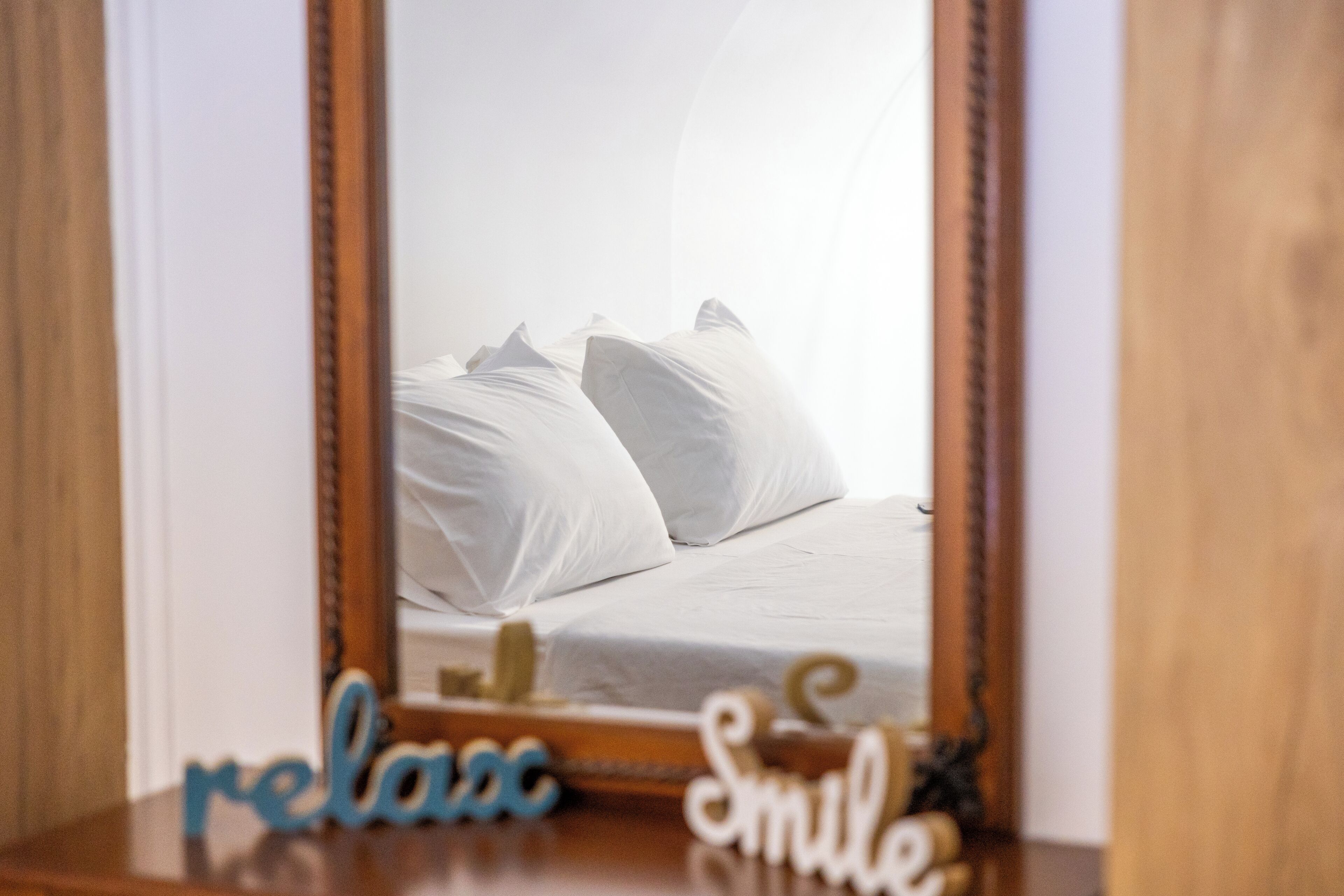 A bedroom with a bed, pillows, and a mirror reflecting the room.