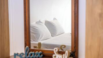 A bedroom with a bed, pillows, and a mirror reflecting the room.