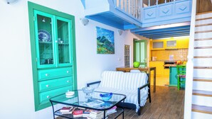 A room with a glass coffee table, a striped sofa, a green cabinet, and a kitchen area with yellow cabinets. - Pitini 2 - Seafront - Harbour view (Symi)