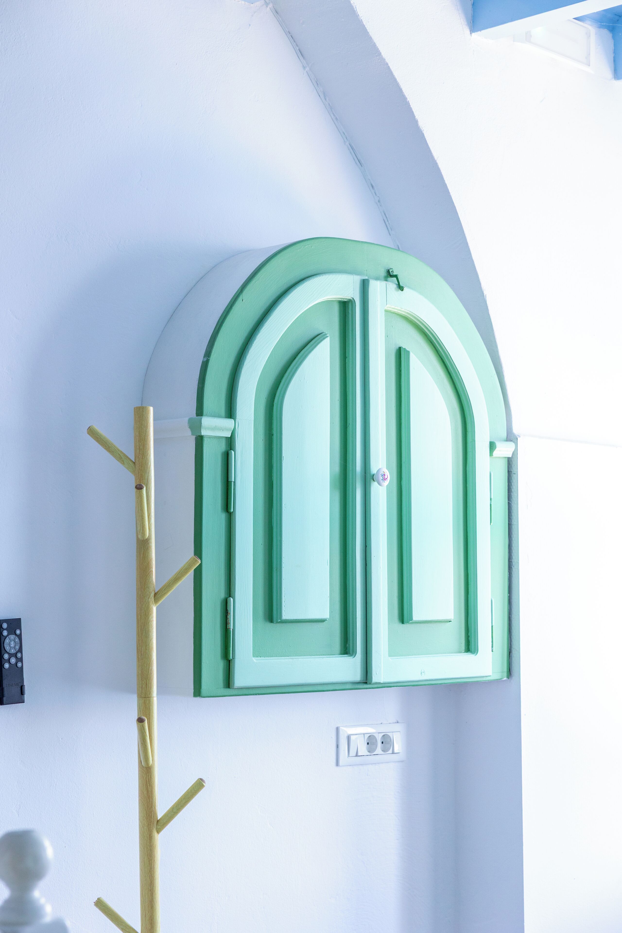 A room with a green arched cabinet and a coat rack.
