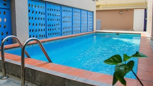 Una piscina con acqua azzurra, circondata da un solarium piastrellato e una recinzione blu con motivi a taglio.