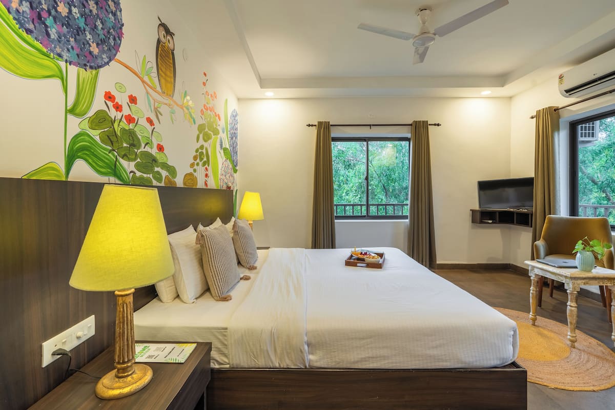 A hotel room with a bed, two bedside lamps, a desk with a laptop, a TV, and a window with curtains.
