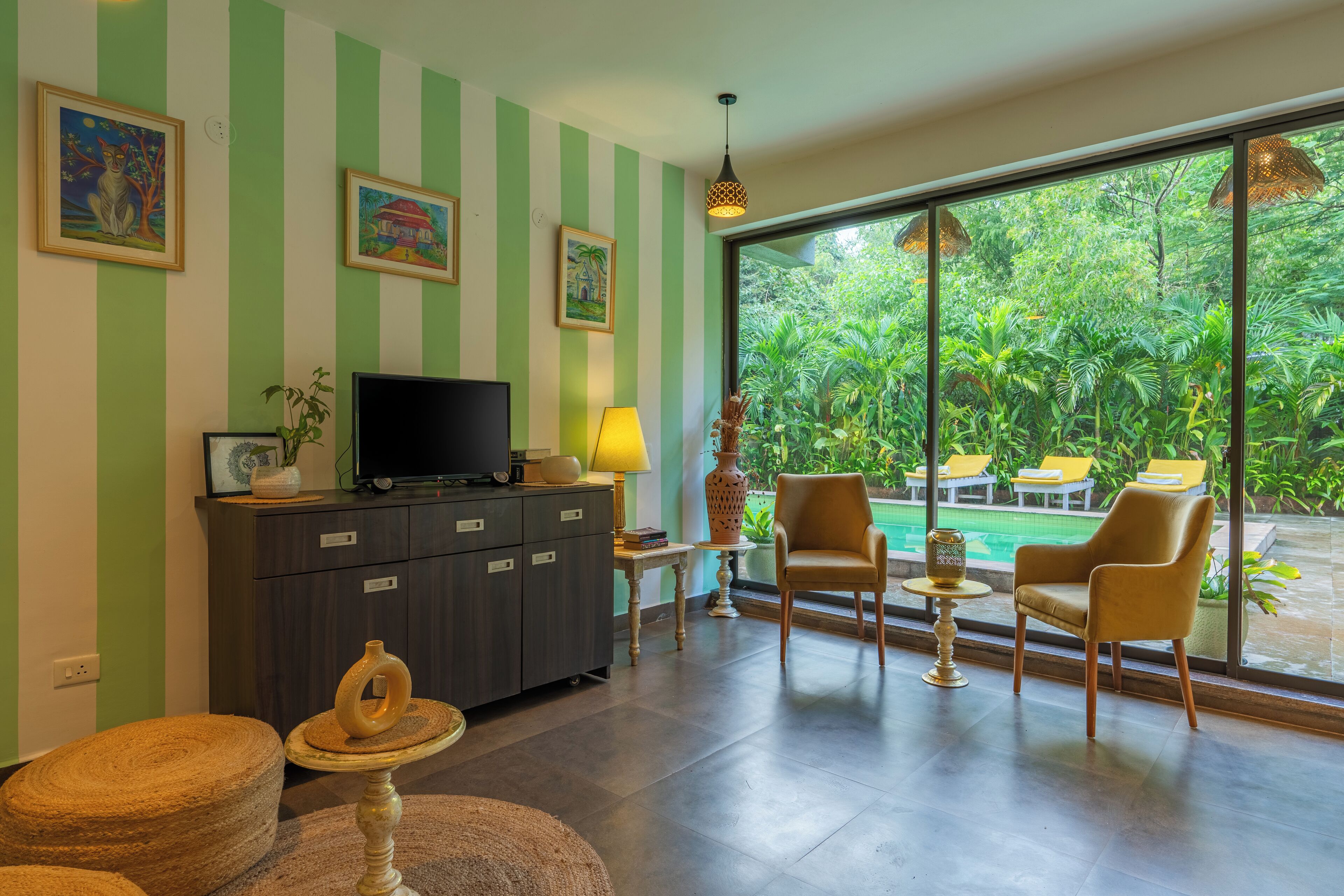 Una sala de estar con televisor, sofá, sillones y vista a una piscina y follaje.