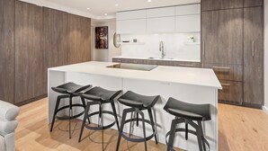 Een moderne keuken met een groot keukeneiland, vier barkrukken en houten keukenkastjes.