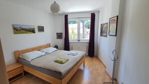 Un dormitorio con cama de madera, una mesita de noche, una ventana con cortinas y una obra de arte en la pared.