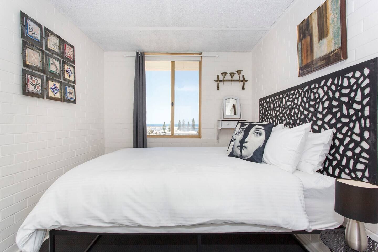 Une chambre avec un grand lit, une vue sur l’extérieur et une tête de lit décorative.
