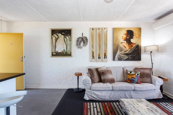 En moderne stue med en hvid murstensvæg, en sofa med pyldere, et sofabord og kunstværker.