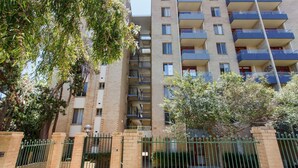 A multi-story residential building with balconies, a gated entrance, and surrounding greenery.