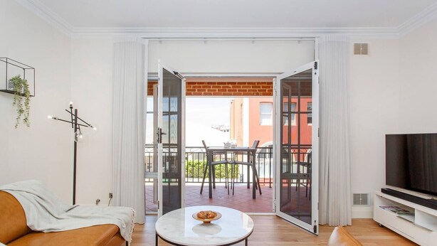 Un salon moderne avec un canapé, une table basse et un téléviseur. Il y a un balcon avec une table et des chaises.