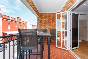 A balcony with a table and chairs, a view of the street, and a brick wall.