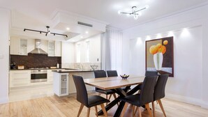 Une cuisine moderne avec des meubles blancs, un îlot central et un coin repas comprenant une table en bois et des chaises noires.