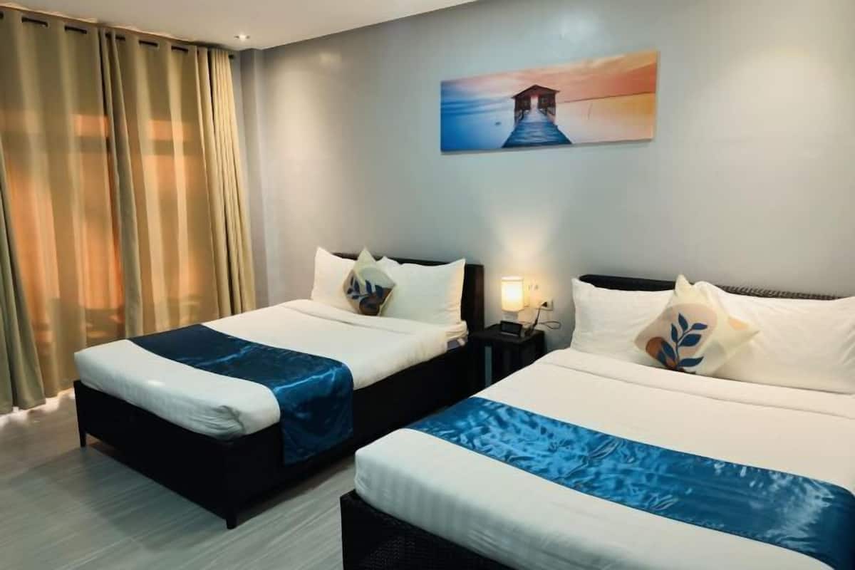 A hotel room with two beds, a nightstand, a lamp, and a painting on the wall.