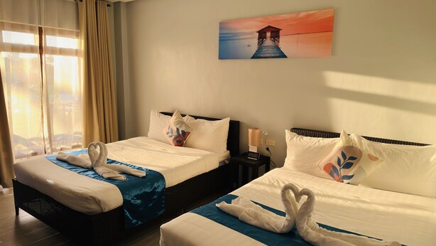 Habitación de hotel con dos camas, un cuadro en la pared, una mesita de noche con una lámpara y una ventana con cortinas.