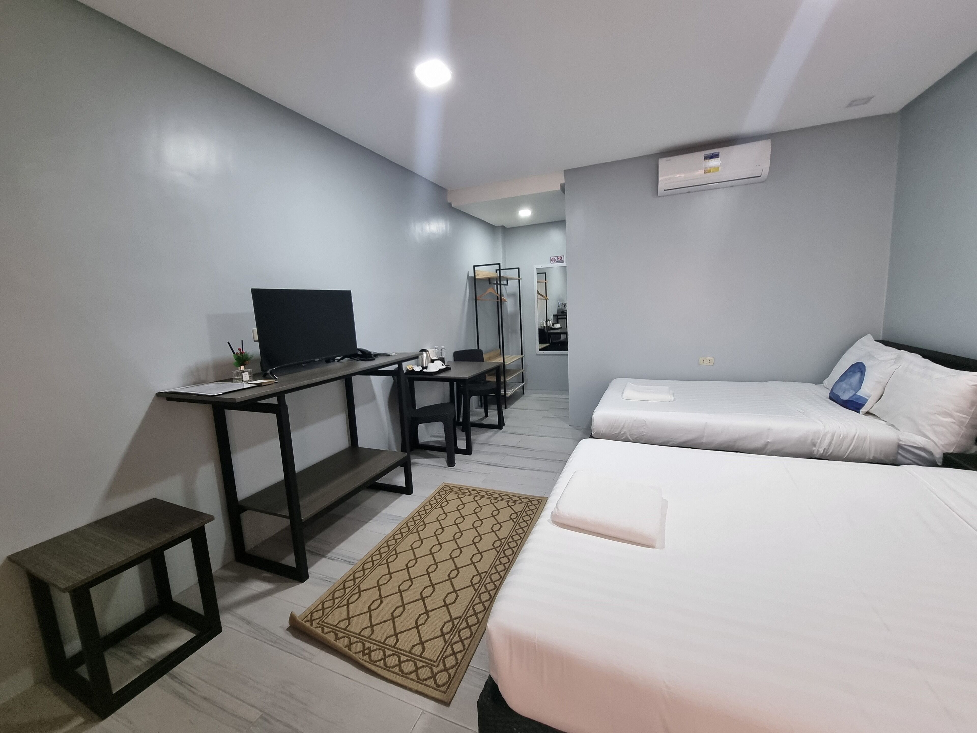 A hotel room with a bed, a desk with a computer, a chair, a small table, a rug, and a wardrobe.