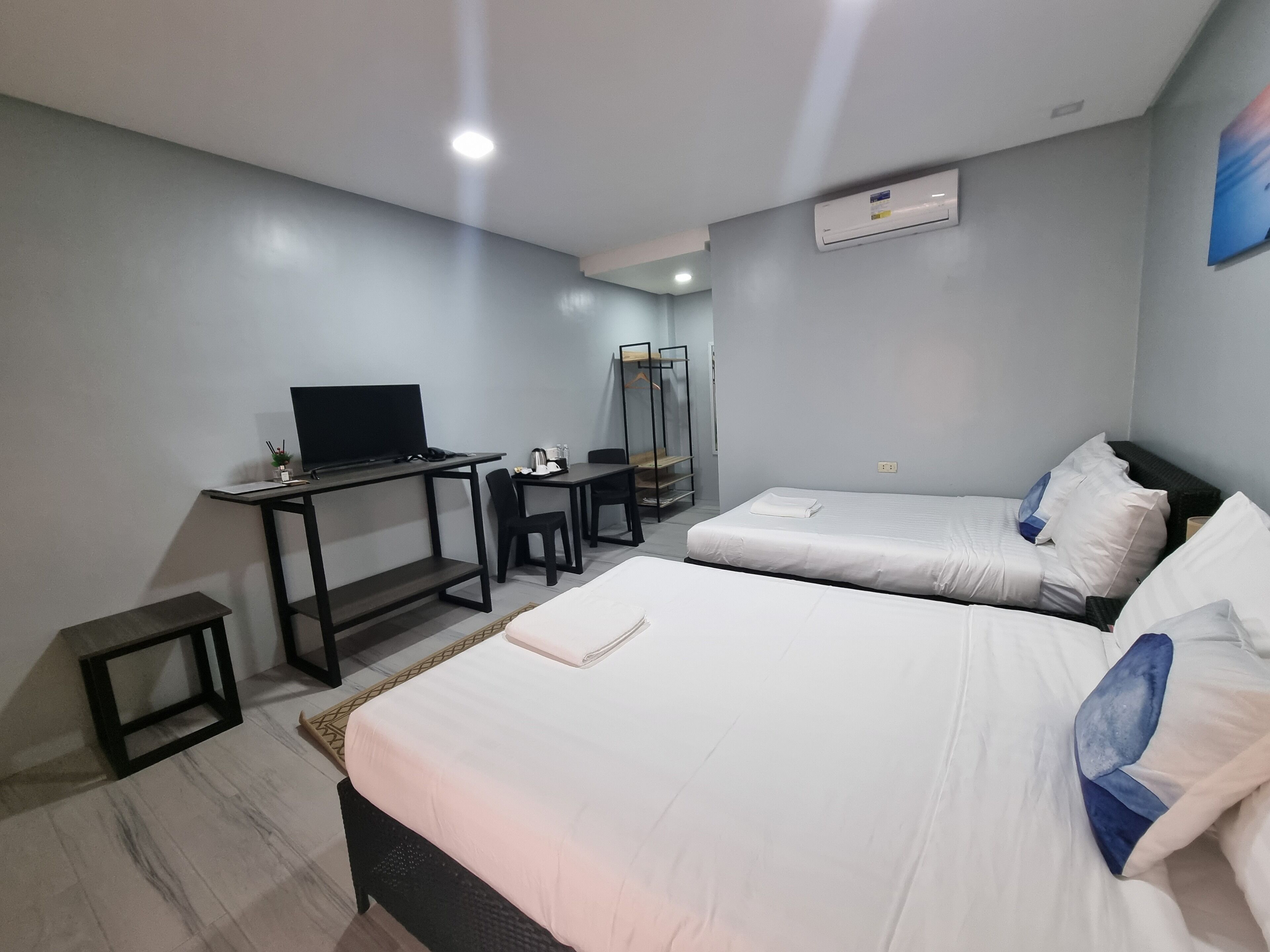 Quarto de hotel com duas camas, uma escrivaninha com computador, uma cadeira, televisão e guarda-roupa.