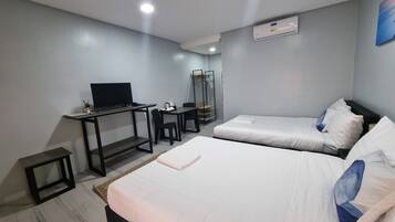 Quarto de hotel com duas camas, uma escrivaninha com computador, uma cadeira, televisão e guarda-roupa.