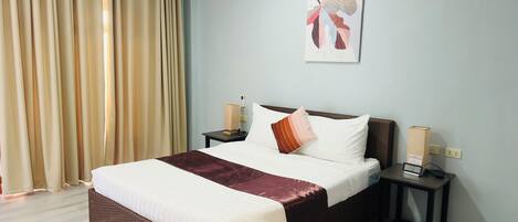 A hotel room with a large bed, a bedside table with a phone and a clock, a wall-mounted artwork, and a window with curtains.