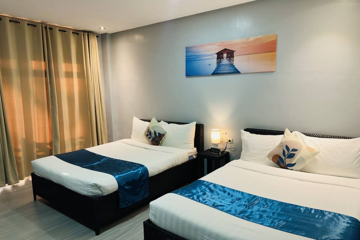 A hotel room with two beds, a painting of a pier, and a nightstand with a lamp.