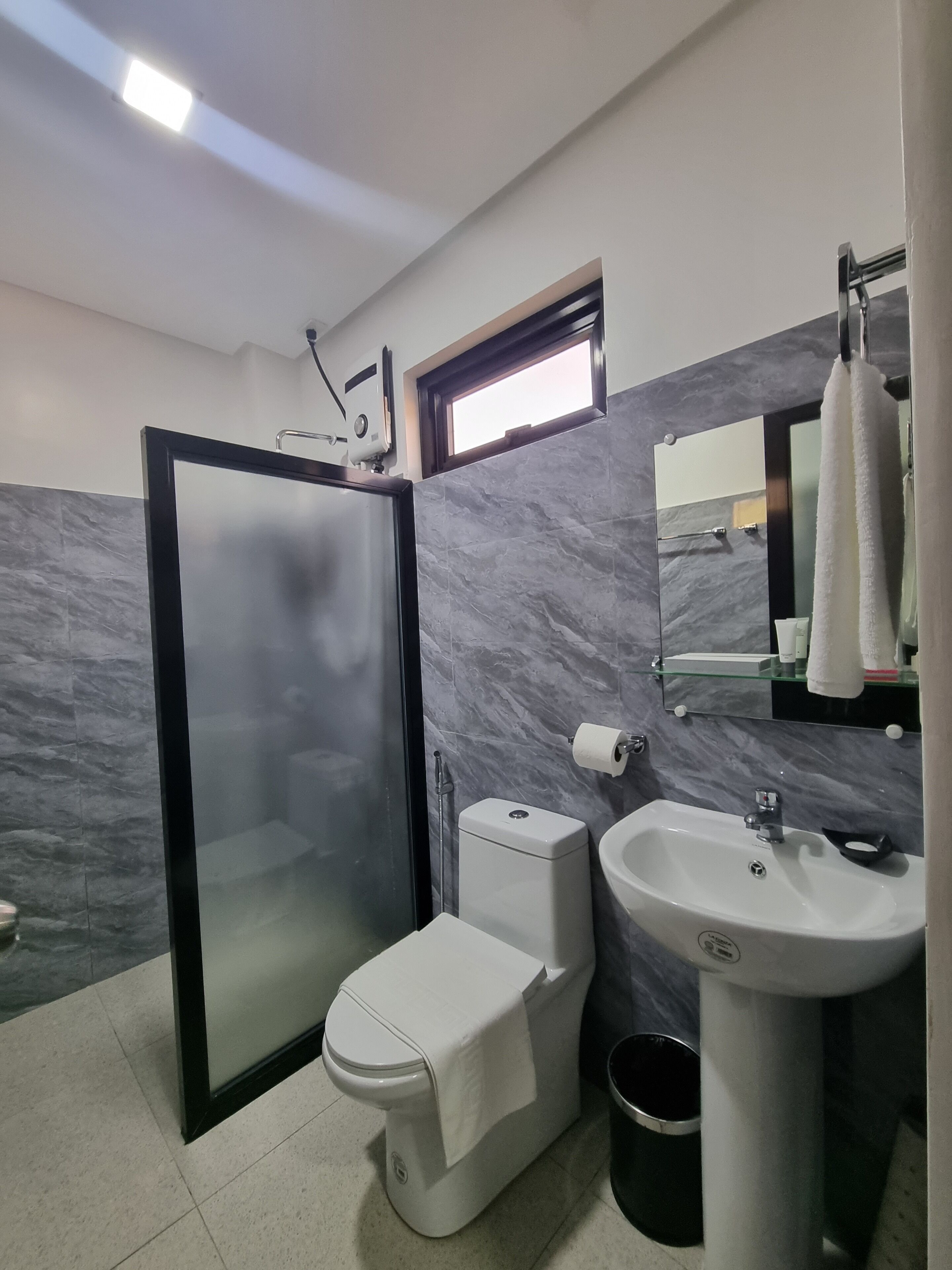 A modern bathroom with a glass-enclosed shower, a toilet, a sink, and a small window above the toilet.