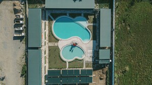 Vista aérea de un hotel con dos piscinas, un área de estacionamiento y un edificio con techo verde.