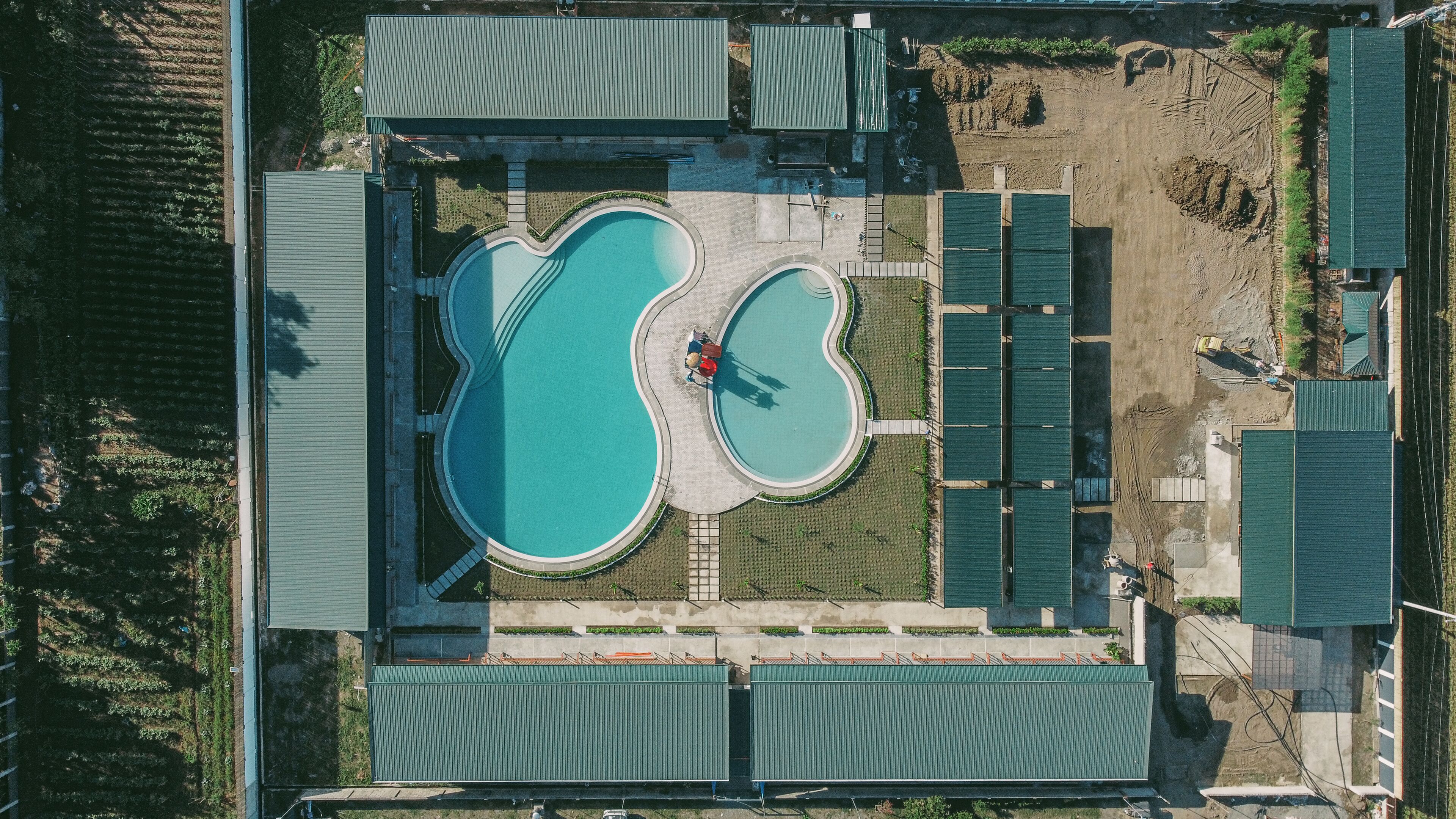 Vista aérea de un complejo turístico con dos piscinas, una cancha de tenis y una zona de estar cubierta.