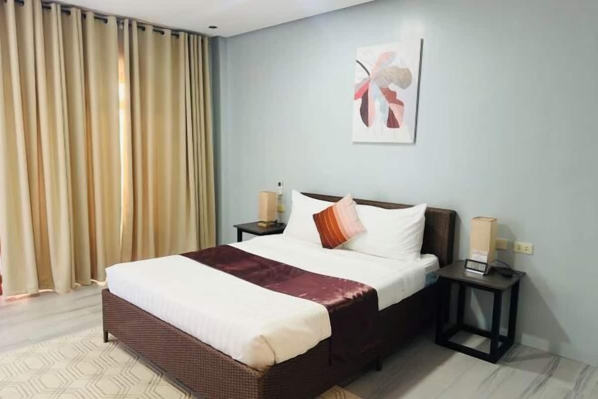 A hotel room with a large bed, a nightstand, a wall-mounted artwork, and a window with curtains.