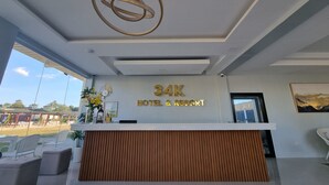 Un área de recepción de diseño moderno, que incluye un mostrador de madera, un gran logotipo circular en el techo y un letrero con el nombre del hotel '34K HOTEL & RESORT'.