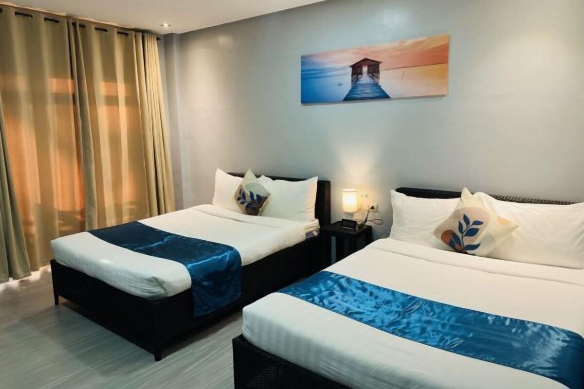 A hotel room with two beds, a nightstand, a lamp, and a painting on the wall.