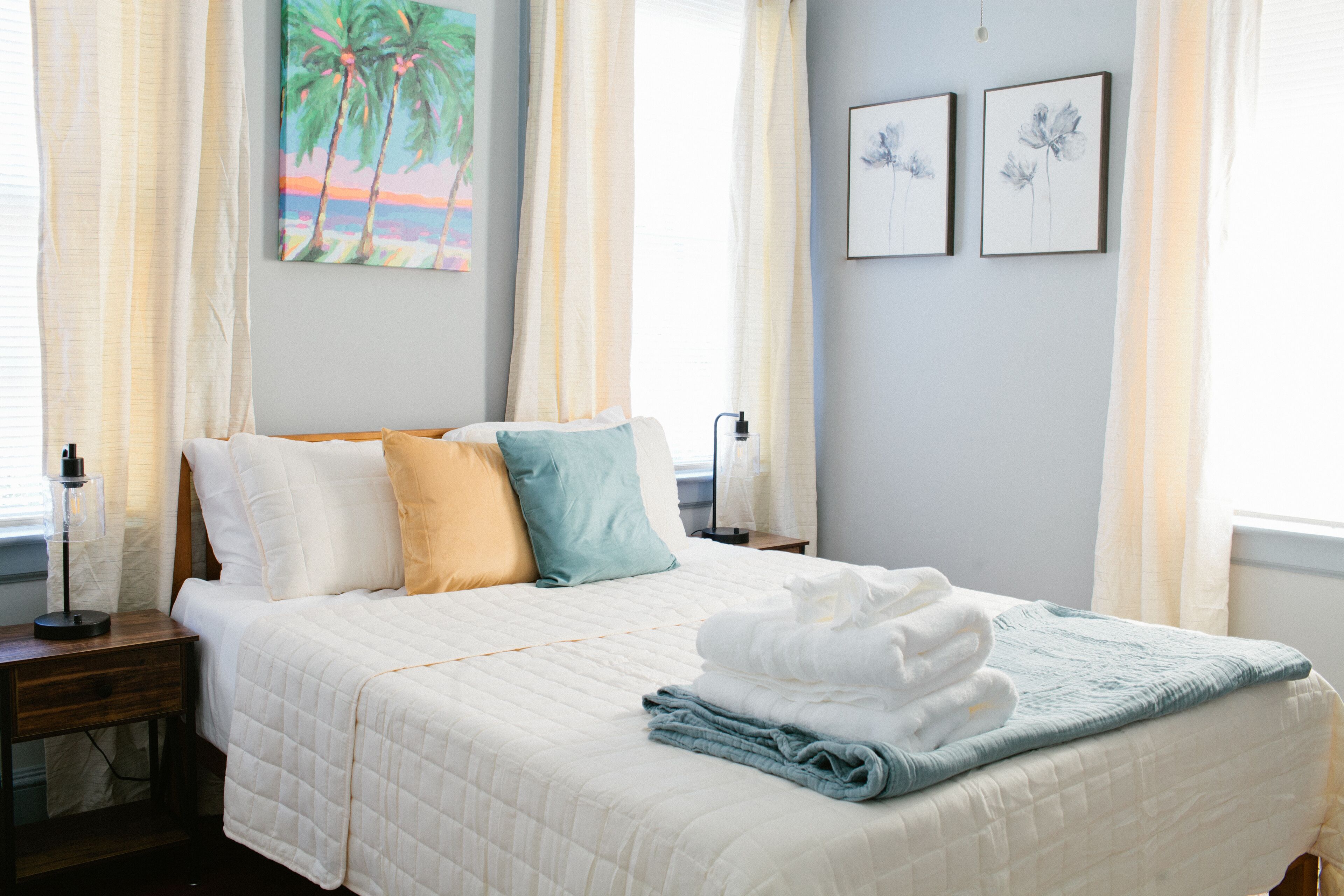 A neatly made bed with a quilted white duvet, blue and yellow pillows, and a folded white towel on top.