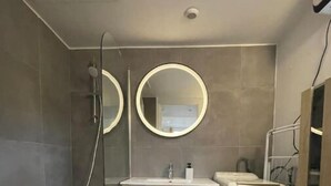 Een moderne badkamer met een bad, een wastafel en een toilet. Boven de wastafel hangen twee ronde spiegels en links is een douchekop.