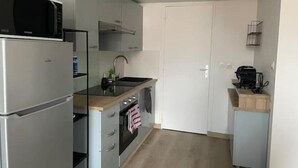 Een kleine keuken met een koelkast, oven, magnetron, spoelbak en een klein aanrecht met een koffiezetapparaat.