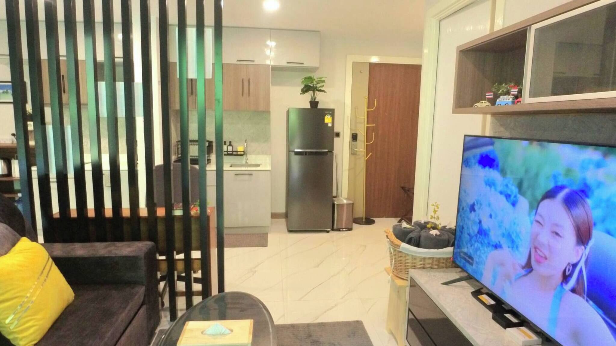 Uma sala de estar moderna com um sofá, uma televisão e uma cozinha ao fundo.